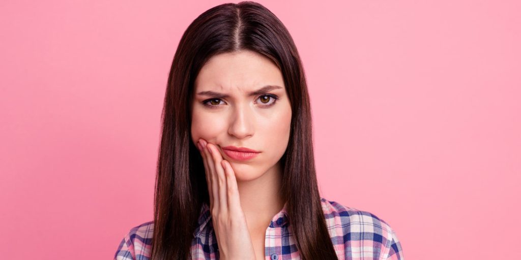 Brunette woman in a plaid shirt cringes and frowns because of her braces pain