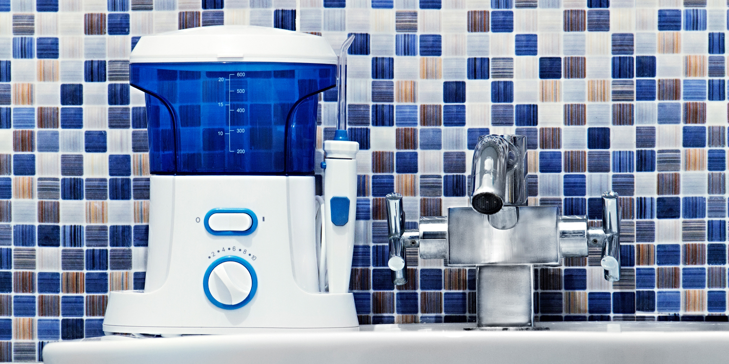 Closeup of a water flosser on a white sink against a blue mosaic backsplash
