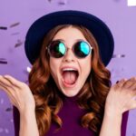 Brunette woman in a black hat and sunglasses celebrates with purple confetti getting her braces off