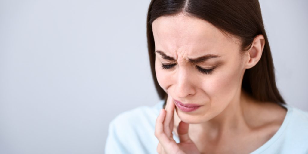 Brunette woman touches her cheek due to braces pain