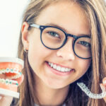 Brunette girl with glasses compares braces with clear aligners for her orthodontic treatment