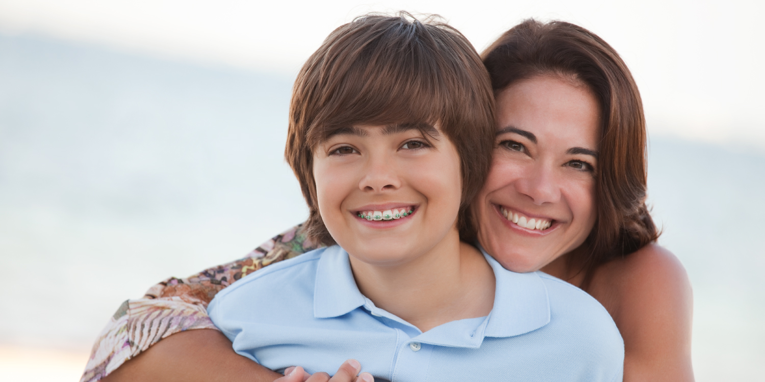 Brunette boy with braces smiles on the beach with his brunette mother