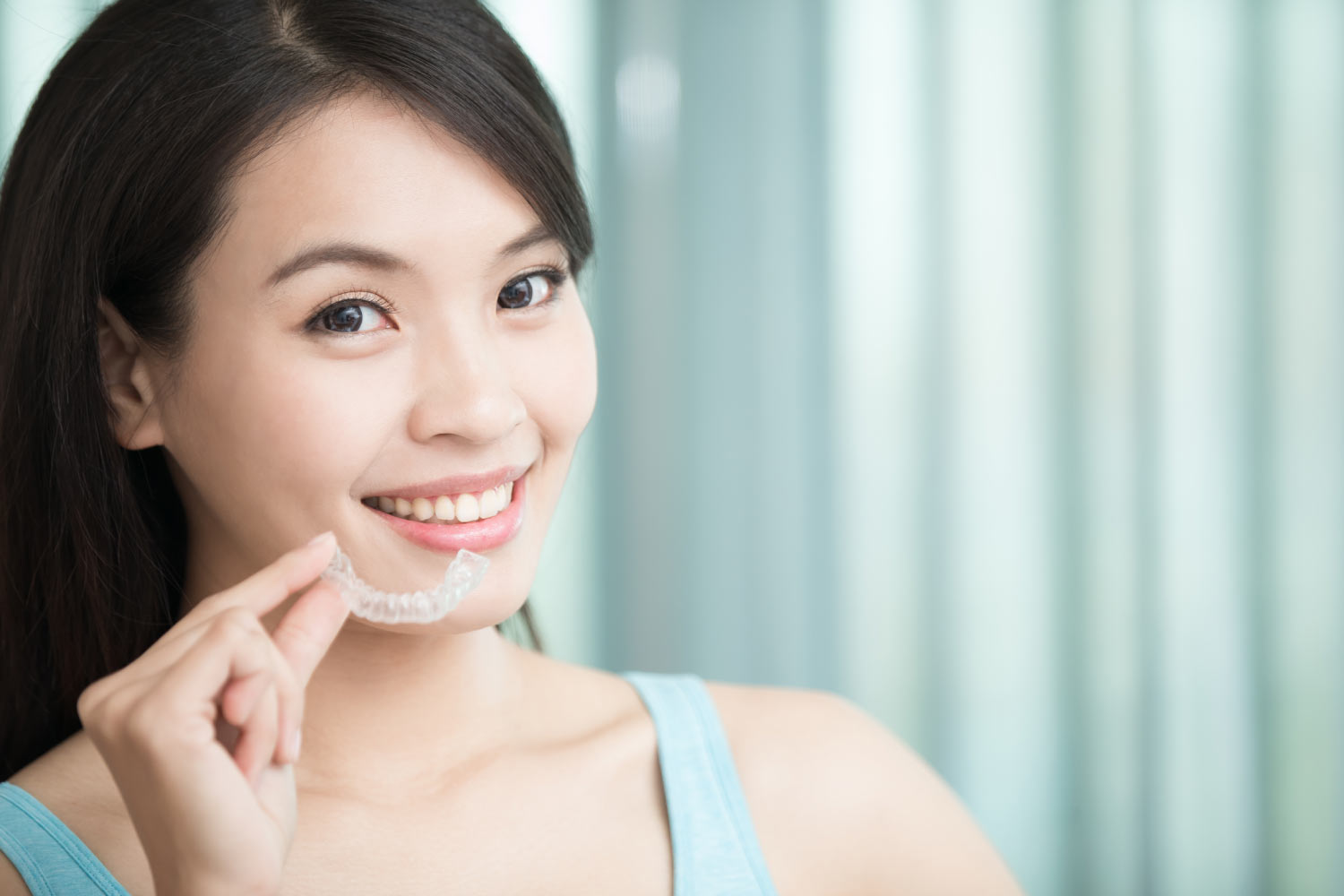 Brunette woman smiles as she holds her Invisalign clear aligners in Weatherford, TX