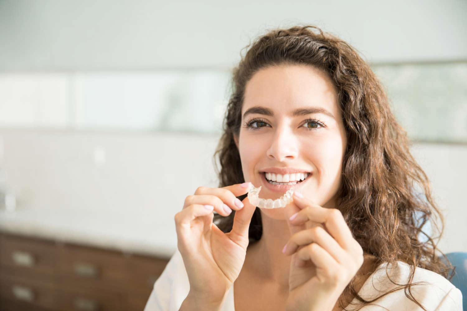 Brunette smiling woman holding a clear aligner.