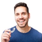 A smiling man holds a clear aligner.