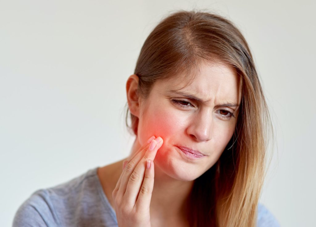 closeup of a young woman cringing in pain and touching her cheek with a red hotspot due to a pokey braces wire