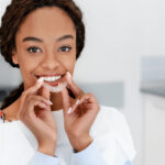 Black woman smiles while putting in her clear aligners at her orthodontist in Weatherford, TX