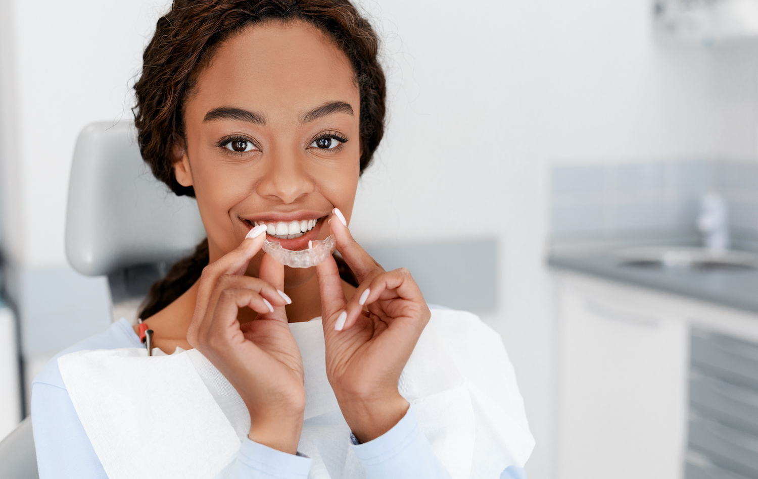 Black woman smiles while putting in her clear aligners at her orthodontist in Weatherford, TX