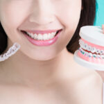 Photograph of woman comparing Invisalign clear aligners and traditional braces.