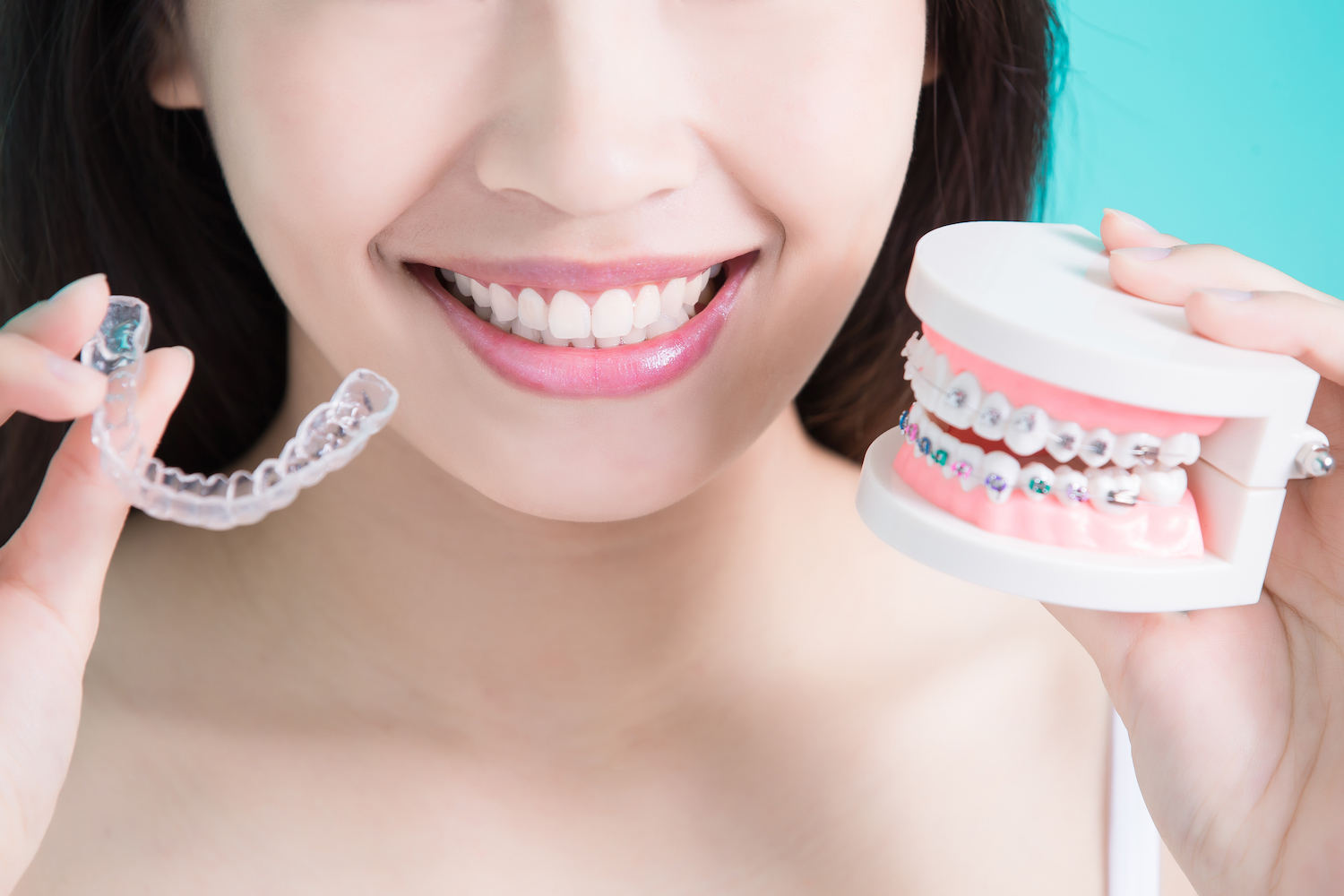 Photograph of woman comparing Invisalign clear aligners and traditional braces.