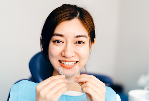 woman at dentist holding up a clear aligner